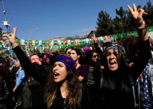 Dos mujeres en una gran manifestación, ellas están en primer plano y tienen las manos levantadas con el signo de victoria